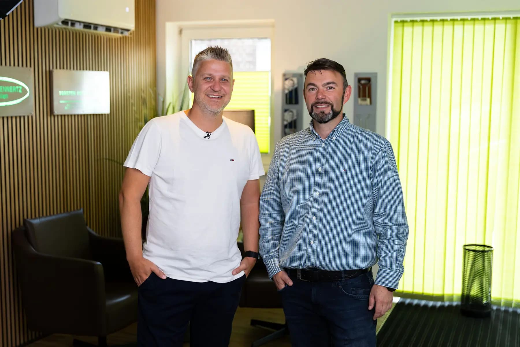 Torsten Kotzan und Markus Sattler stehen nebeneinander in einem Büro mit Holzlattenwand