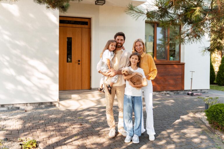 Familie mit Kindern und Hund steht vor modernem Eigenheim nach erfolgreicher Baufinanzierung