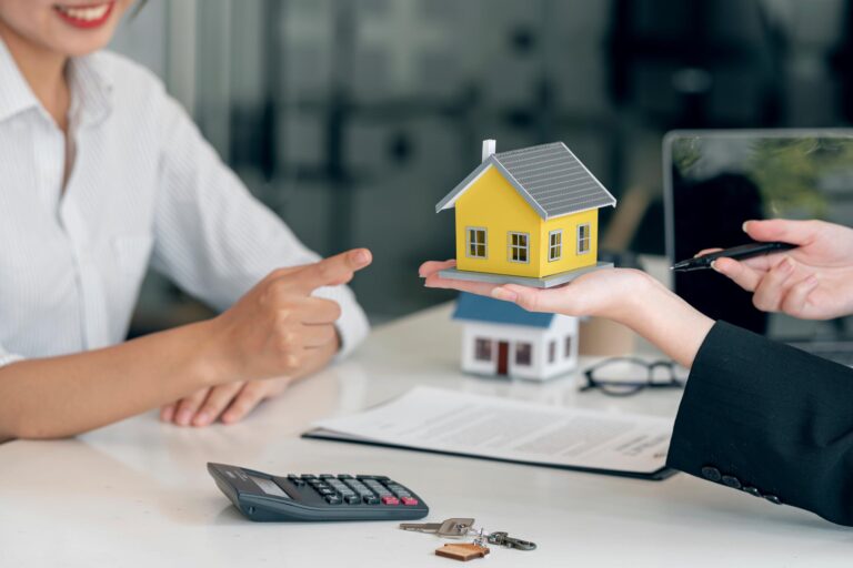 Beratung zur Baufinanzierung: Hände halten Modellhaus bei Kreditgespräch