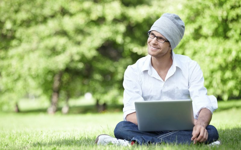 Ein Mann sitzt im Stadtpark mit einem Notebook im Schoss